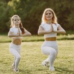 A mother and daughter practicing yoga together in matching outfits in a sunny park.