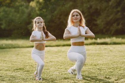 A mother and daughter practicing yoga together in matching outfits in a sunny park.