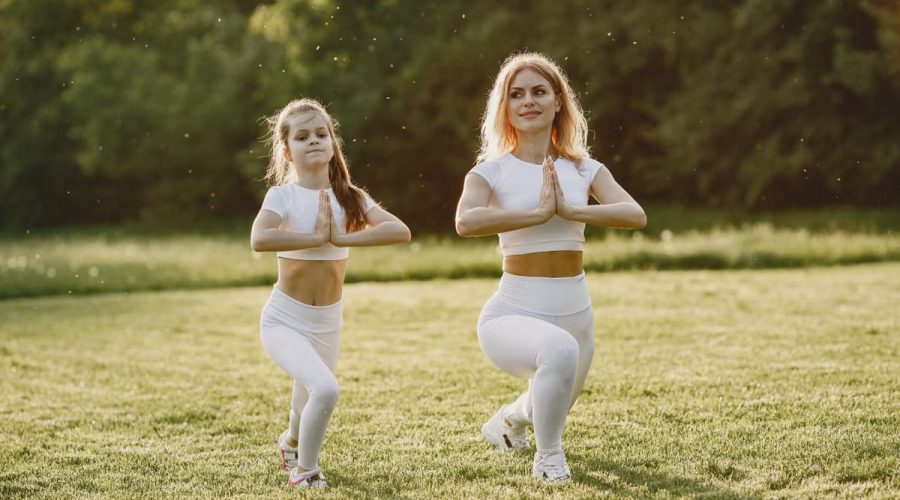 A mother and daughter practicing yoga together in matching outfits in a sunny park.